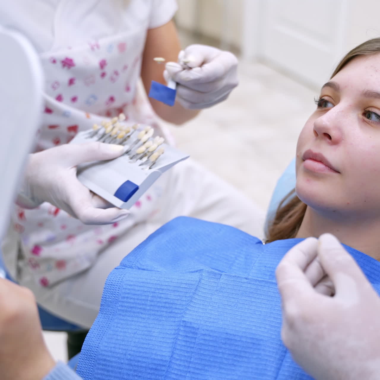 Smiling female patient at dentist's. Stomatologist Choosing the color of tooth to a pretty woman in clinic. Tooth whitening chart.