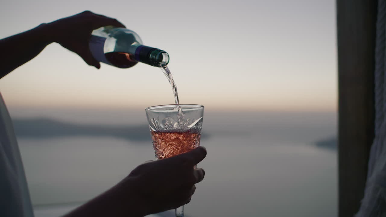 verter vino en un vaso cortado con caldera y fondo marino al atardecer - primer plano en cámara lenta, thira, santorini