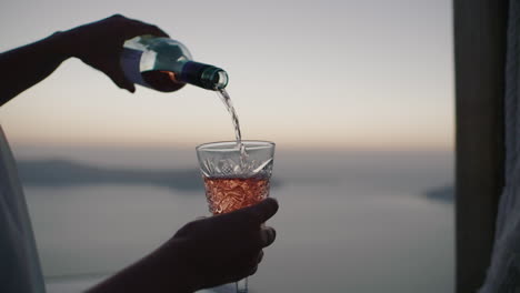 Pouring-wine-into-a-cut-glass-with-Caldera-and-sea-background-at-sunset---Slow-motion-Close-up,-Thira,-Santorini