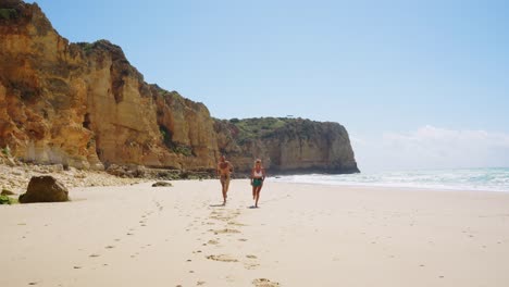 couple holding hands, running in the scenic beach in summer in algarve, portugal. - wide shot