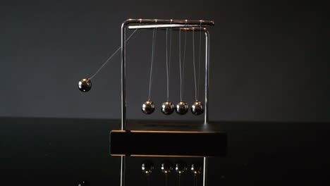 closeup video of metal newton cradle swinging on gray background