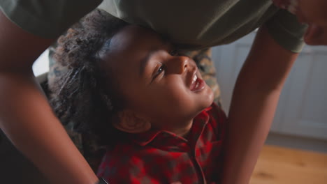 army mother in uniform home on leave playing with son in family kitchen