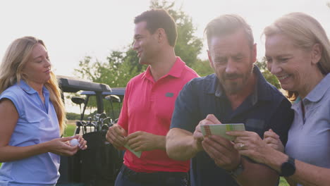 mature and mid adult couples standing by golf buggy checking score cards together