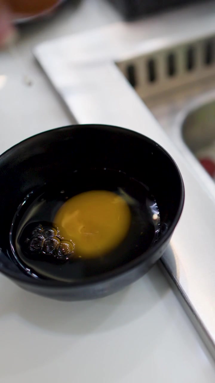 Close-up shot of hands cracking a fresh egg into a black bowl at a restaurant