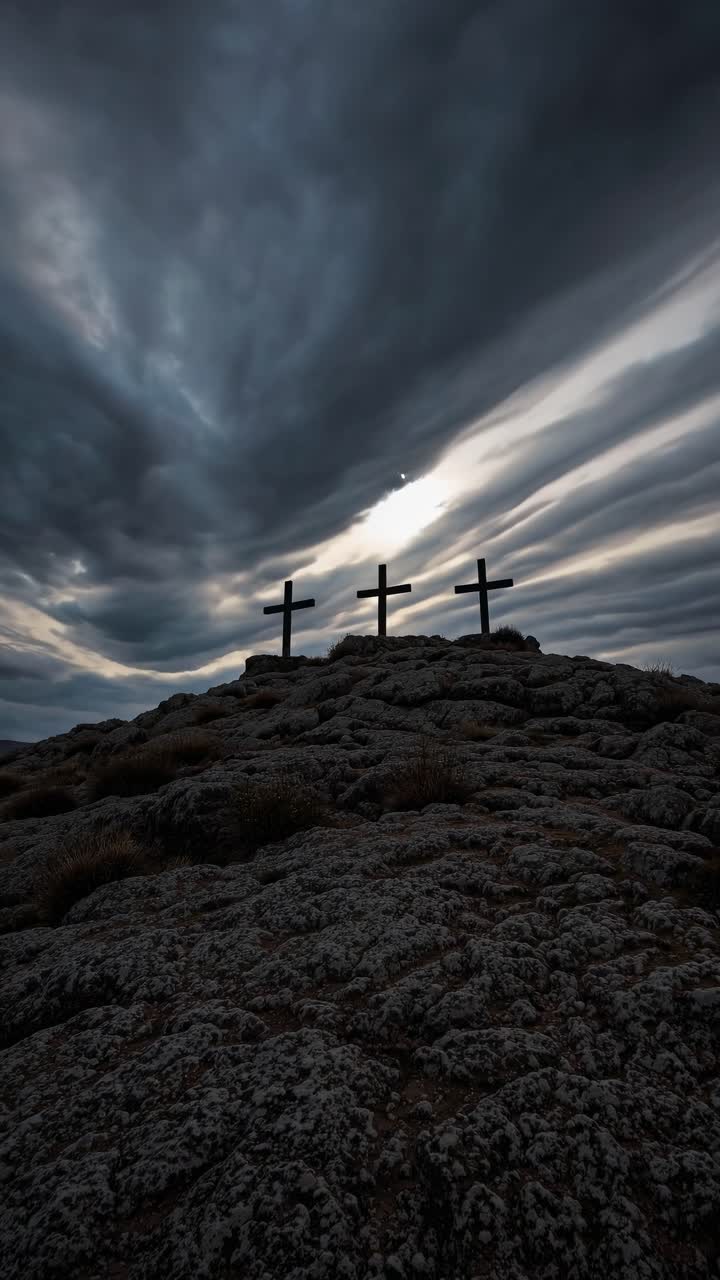 Dramatic low-angle shot of three crosses on a rocky hill under a moody sky, creating a cinematic