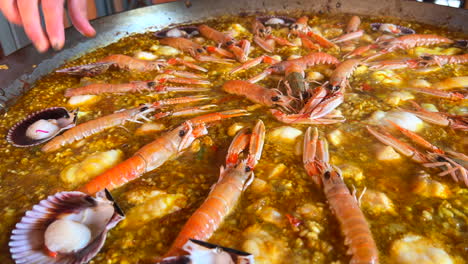 cooking a big traditional spanish seafood paella dish with shrimps, st jacques scallops and cigala norway lobsters nephrops norvegicus, cooked rice with seafood, marbella spain, 4k shot