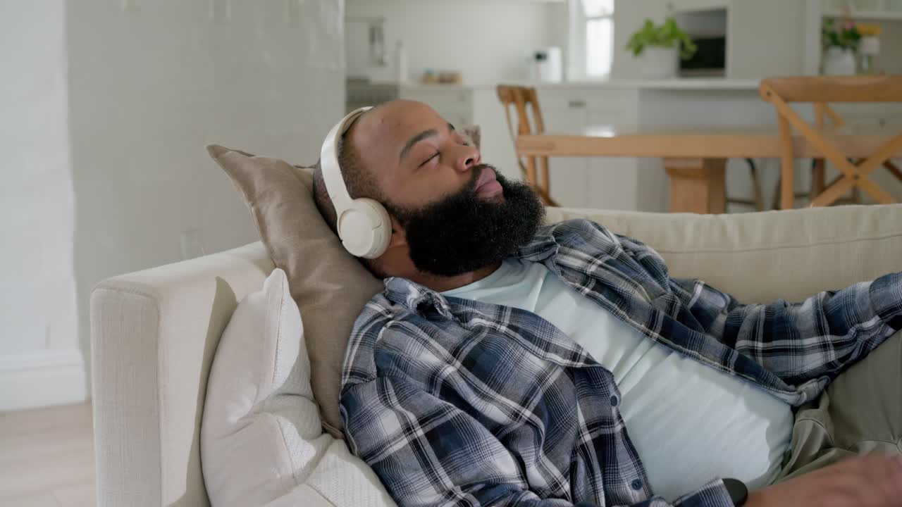 Uomo afroamericano che abbassa il telefono rosa, appoggiato a un cuscino, chiude gli occhi e ascolta con le cuffie.