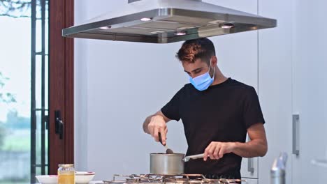 young man at home preparing food with protective mask