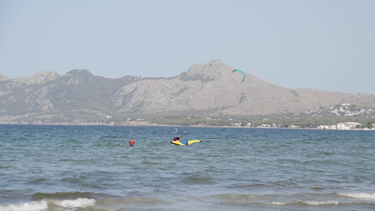 Mallorca Balear Adaları'nda, dağlarla çevrili berrak mavi sularda kiteboard ve wingfoil sörfçüsü.