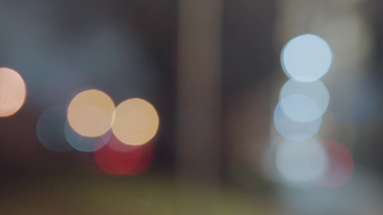 Luci notturne bokeh sfocate, bagliore soffuso della città, traffico distante e lampioni resi come riflessi circolari colorati, atmosfera nebbiosa, profondità di campo ridotta, atmosfera cinematografica, luccichio ambientale ideale per sfondo