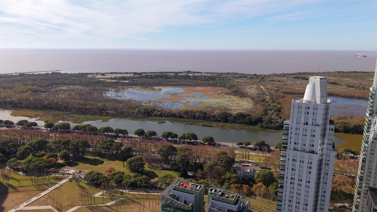 Aerial push-in shot from the modern skyscrapers of Puerto Madero towards the Costanera Sur Ecological Reserve and Rio de la Plata in Buenos Aires