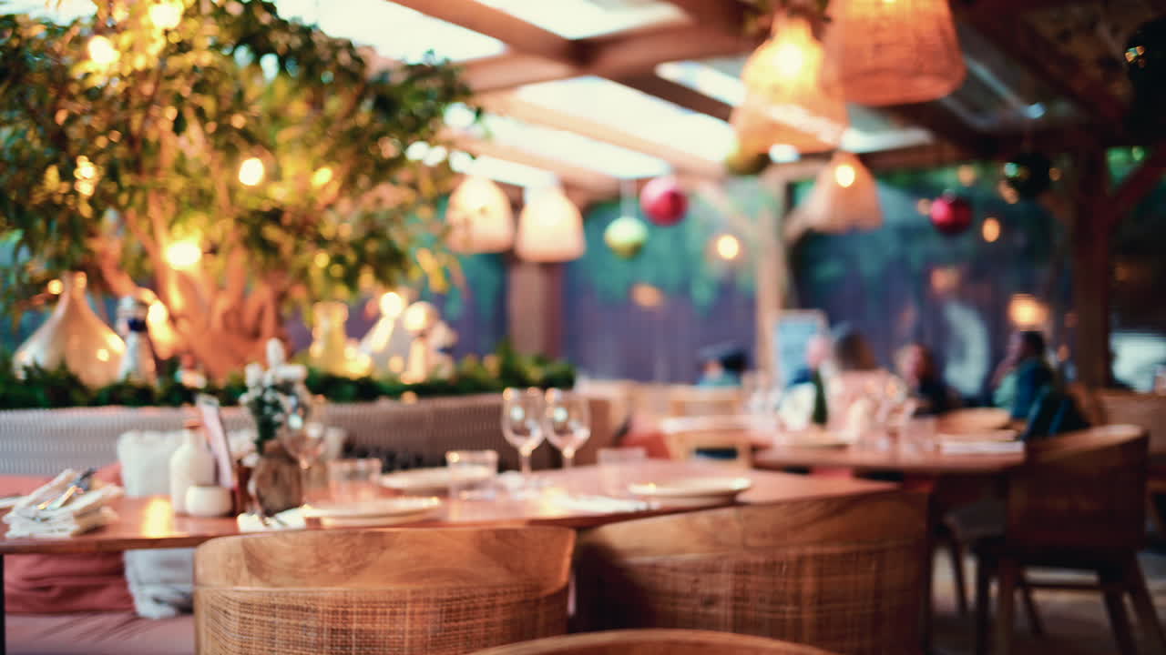 Campo lungo dell'interno di un ristorante con tavoli e sedie in legno, luci sospese e piante decorative
