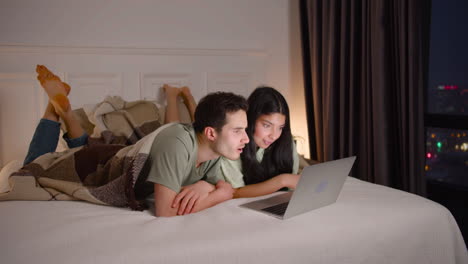 couple watching interesting movie on laptop lying in bed at home