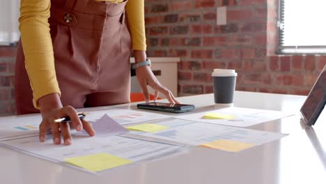 Midsection-of-african-american-casual-businesswoman-looking-at-documents-in-office,-slow-motion