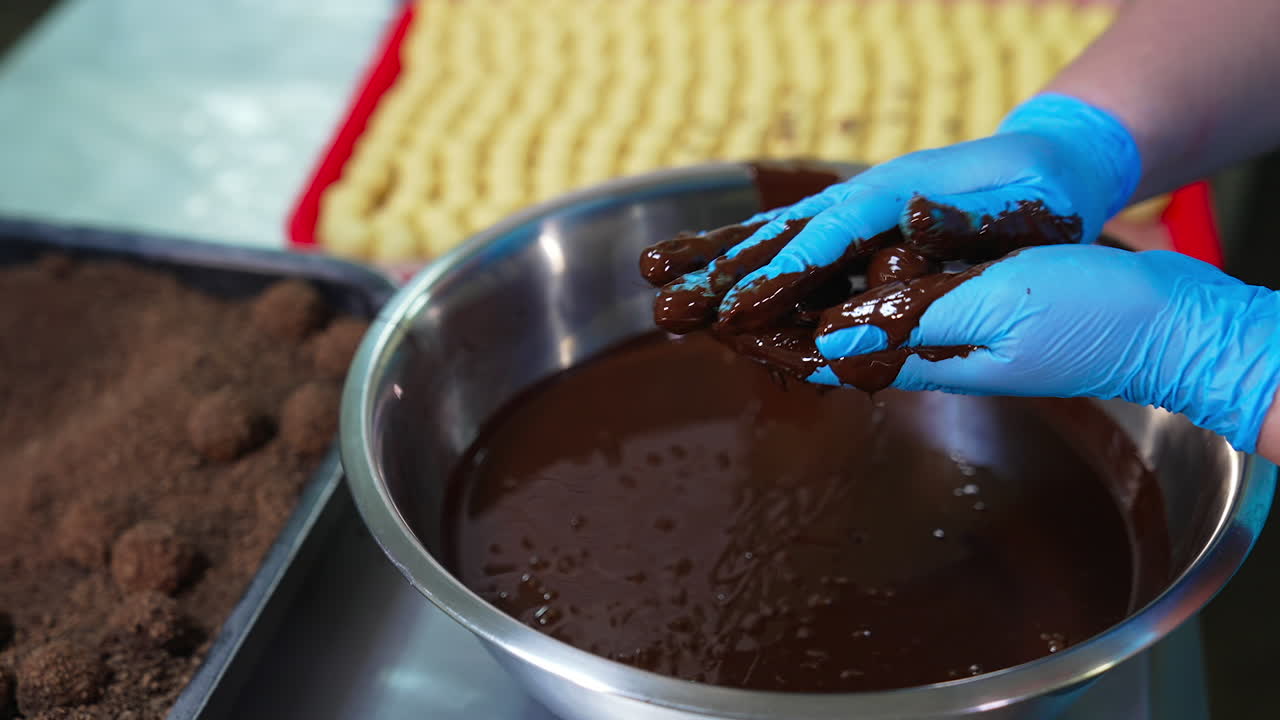 Confectioner's hands cover candies with layer of chocolate. Handmade manufacturing of chocolate candies. Close up.