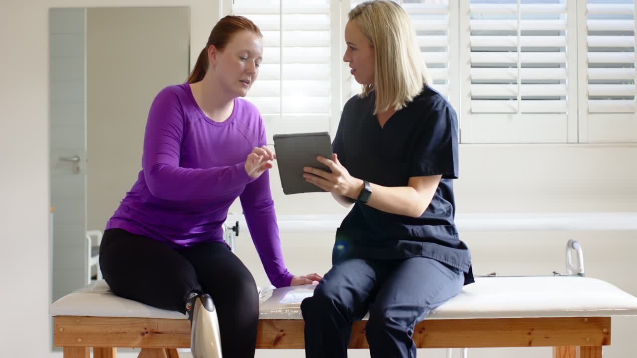 Discussing prosthetic options, woman with prosthetic leg consulting therapist using tablet