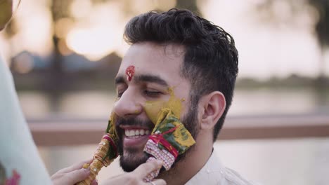 mujer aplicando cúrcuma en la cara del novio durante la ceremonia haldi - cerrar