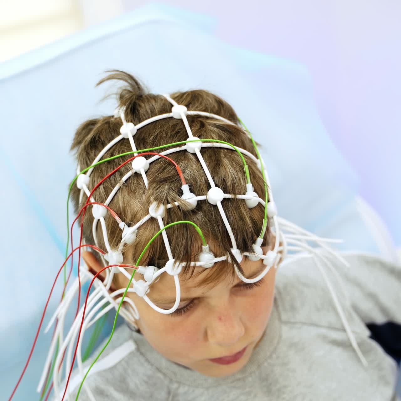 Preparing little Caucasian boy for the electroencephalographic examination. Medic in blue gloves attaching the electrodes to child's head