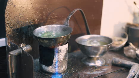 jeweler uses burner to heat green liquid on table closeup