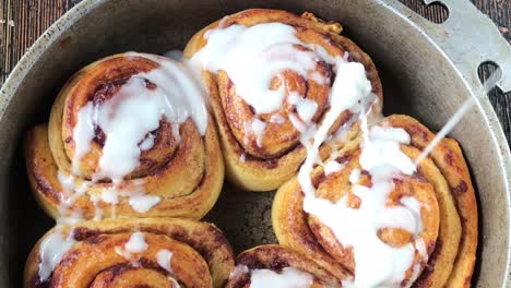 drizzling with white sugar glaze over top of baked cinnamon rolls in pan flat lay