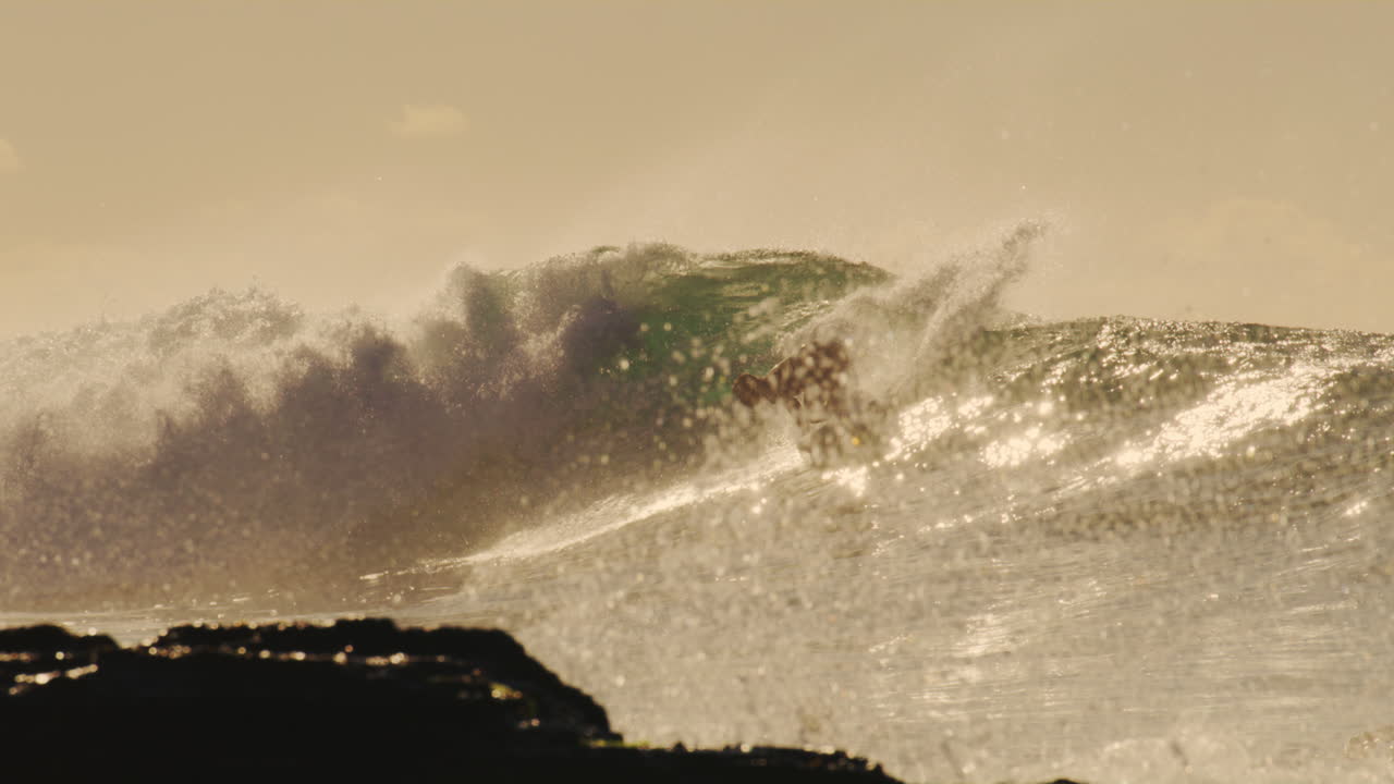 Strong tough water crashes in slow motion with surfer turning and spraying as water erupts across rocks