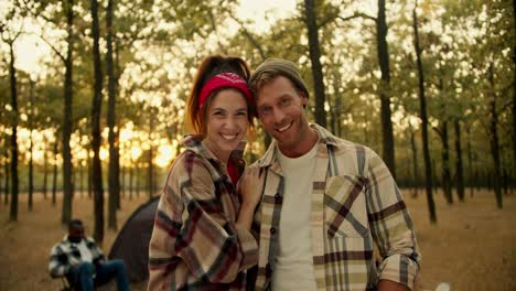 retrato de una pareja feliz, un hombre rubio con paja en una camisa a cuadros y una chica morena en un pañuelo rojo y de pie y mirando a la cámara apoyándose el uno en el otro. pareja feliz durante una caminata en un bosque verde de verano soleado