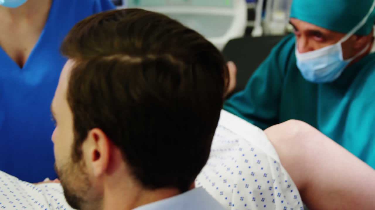 Doctor examining pregnant woman during delivery while man holding her hand in operating room