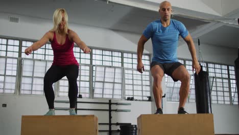 fit caucasian woman and man jumping on pylo boxes at the gym