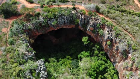 aerial drone rotating medium shot of the large lapa doce cave entrance of colorful rocks with a self-contained rainforest below in the chapada diamantina national park in bahia, northeastern brazil