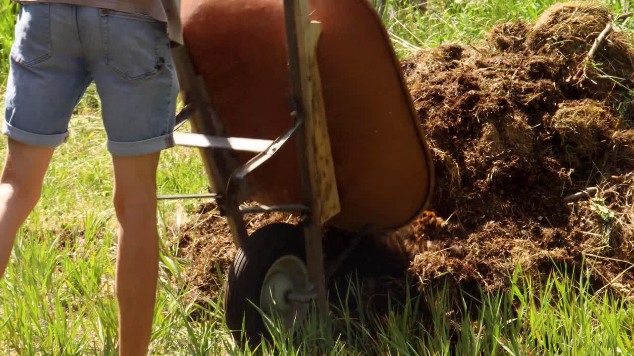 A person dumps a wheelbarrow load of dirt onto a pile