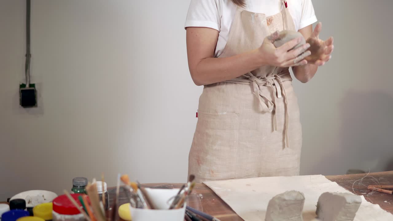Woman sculptor is shaping round blanks from gray clay in workshop