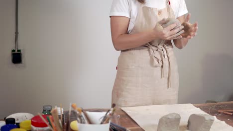 woman sculptor is shaping round blanks from gray clay in workshop
