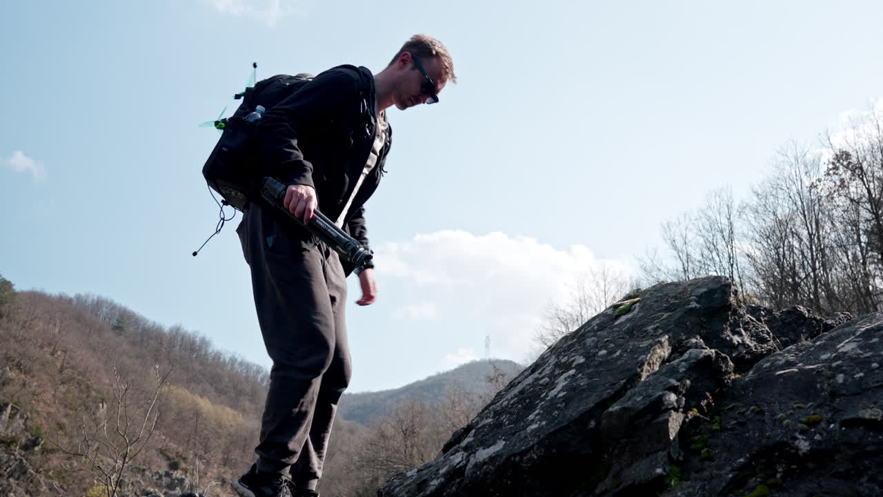Homem caminhando por uma trilha rochosa com mochila, ar puro, em clima de exploração.