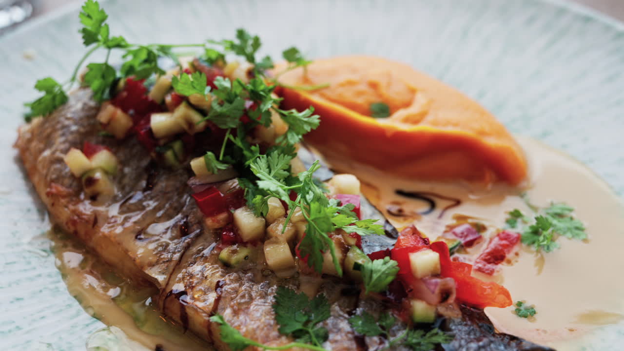 Close up of grilled fish with a sweet potato puree and a sauce on a white plate on a table at a restaurant