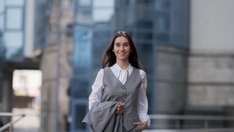 happy young woman in a business suit with a jacket in his hands smiling walking through the city