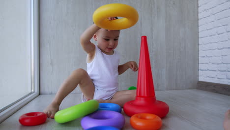 adorable active toddler disassembling toy pyramid. kid cheerfully takes off the colorful rings and puts them on the floor.