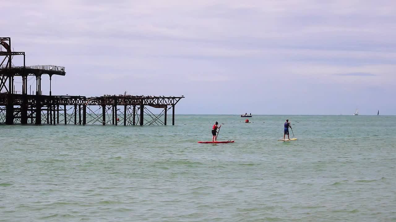 Brighton, England - August 11 2018: A sporting couple using paddle boards as recreation on a sunny day in front of the skeletal burnt out remains of the West Pier in Brighton.