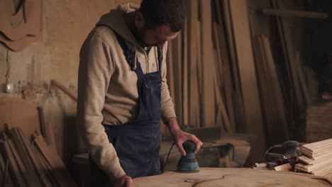 el carpintero en su pequeño taller está trabajando en pulir la pieza de madera. sander. apuntando al disparo