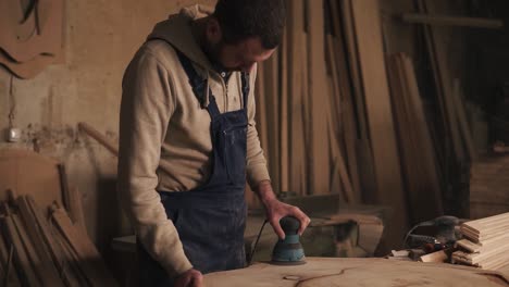 the carpenter in his small workshop is working on polishing the piece of wood. sander. aiming shooting