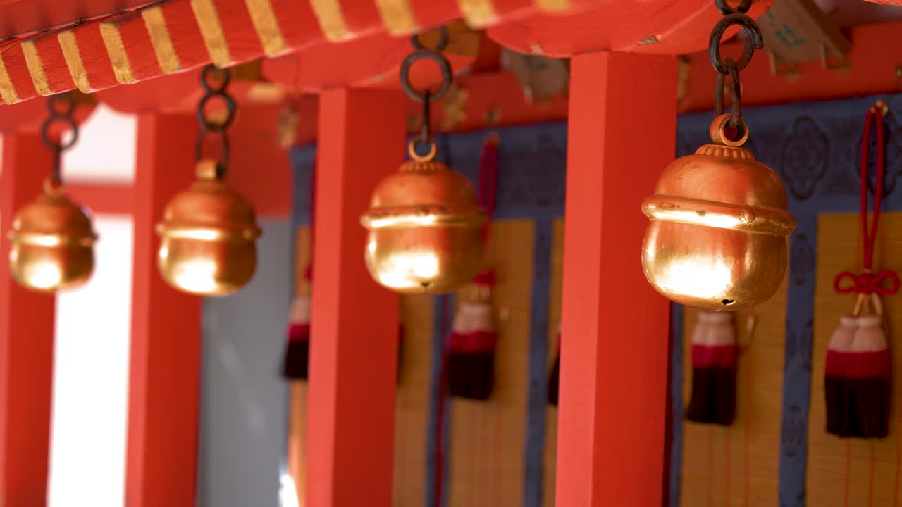Nærbillede af gyldne messingklokker, der hænger fra cinnoberrød træarkitektur ved en japansk helligdom