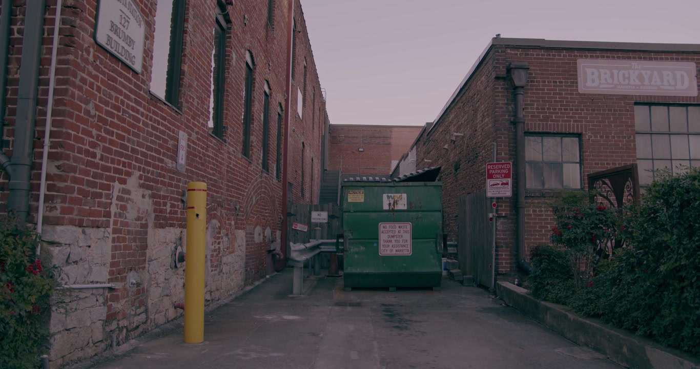 A green trashcan in a small alley