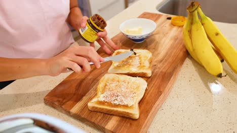 person spreads vegemite on buttered toast in a well-lit kitchen with bananas nearby