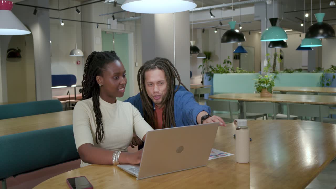 African American coworkers woman typing on laptop reviewing data and man leaning pointing at bottle