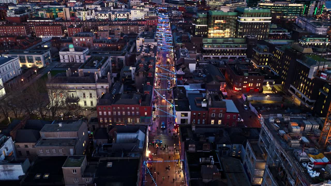 aerial landscape drone shot over O'Connell busy street in Dublin Ireland at twilight blue hour in winter with illuminated streets and busy tourists and cars below walking around the lit streets