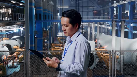 trabajador de fábrica usando una tableta para monitorear robots industriales.