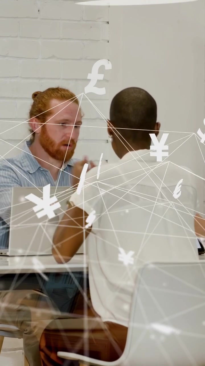 Vertical video: Bearded man at laptop looking up man entering team talking funds symbols overlaying