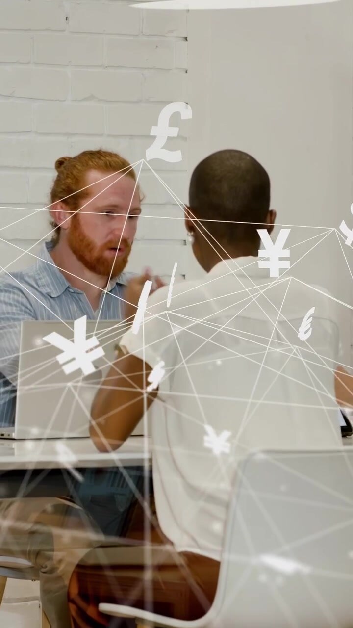 Vertical video: Bearded man at laptop looking up man entering team talking funds symbols overlaying