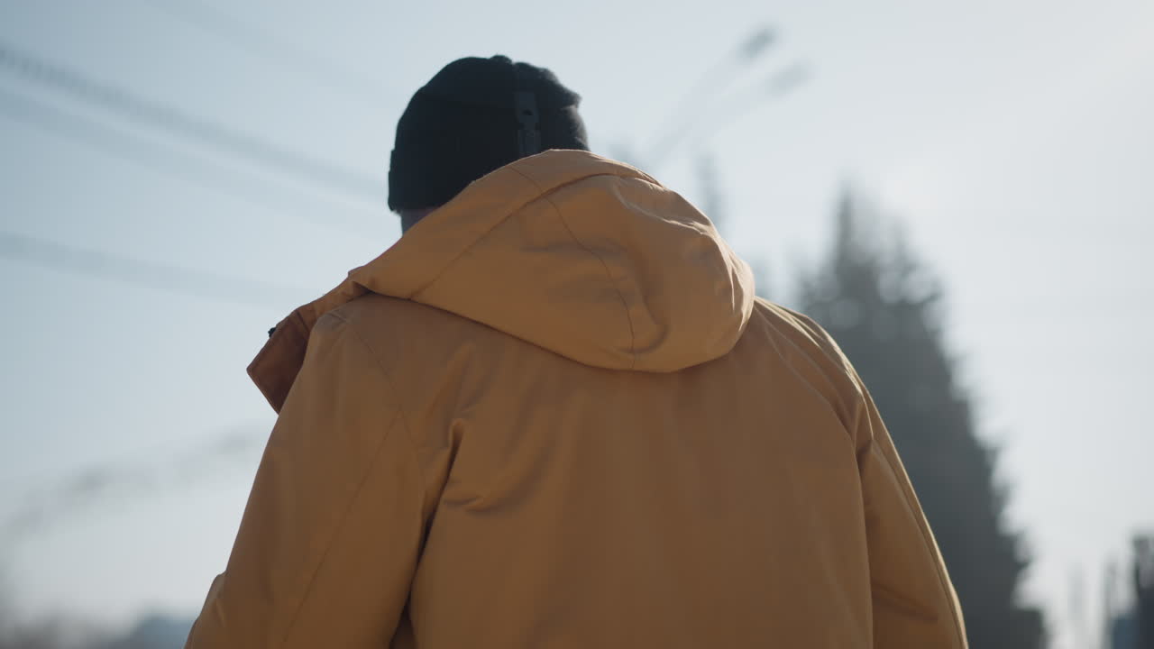 round view of outdoor photographer looking up drinking beverage while holding camera, cars parked and moving along street under soft winter daylight with visible breath in icy air crisp