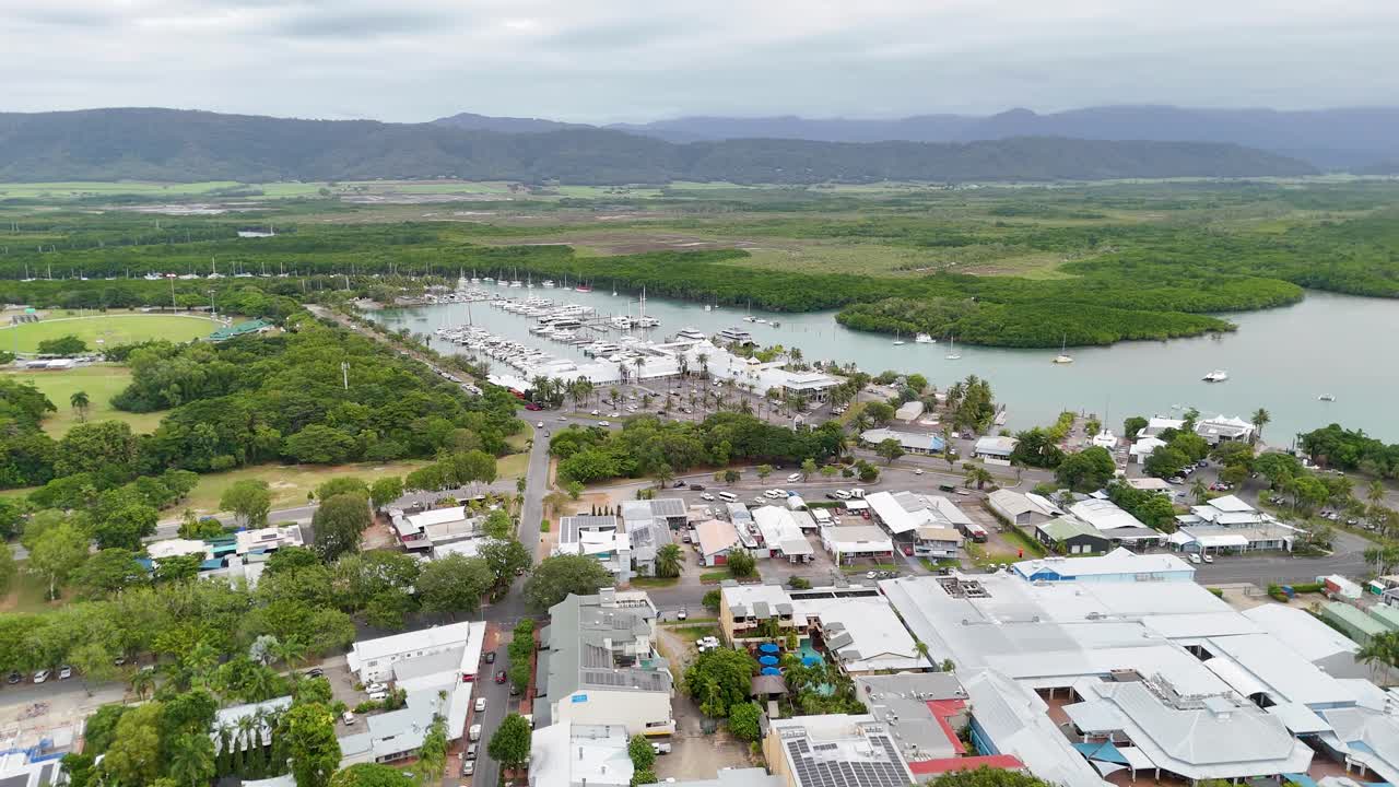 Drone footage captures Port Douglas' marina, lush mangroves, and surrounding landscape under overcast skies, showcasing the town's natural beauty