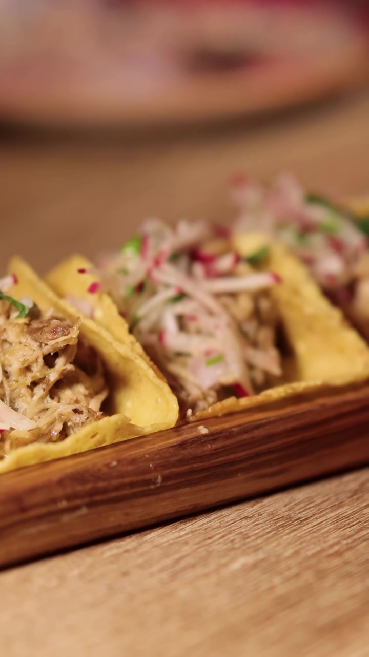 Primo piano di tacos con condimenti vivaci su un vassoio di legno. L'illuminazione calda esalta la presentazione appetitosa in un ristorante di Bangkok.